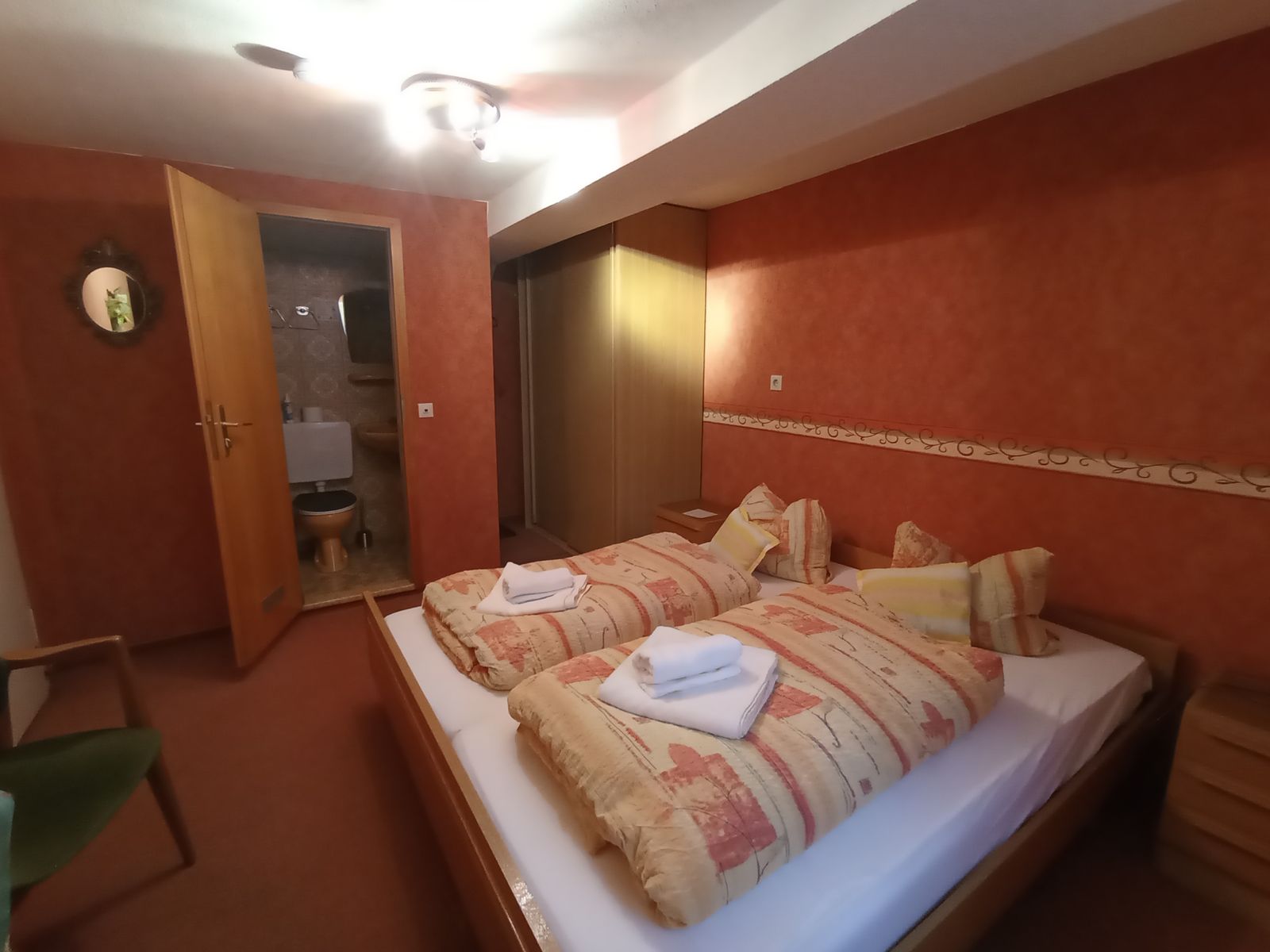 Einzelzimmer mit breitem Bett, Schrank und Tür zum eigenen Duschbad