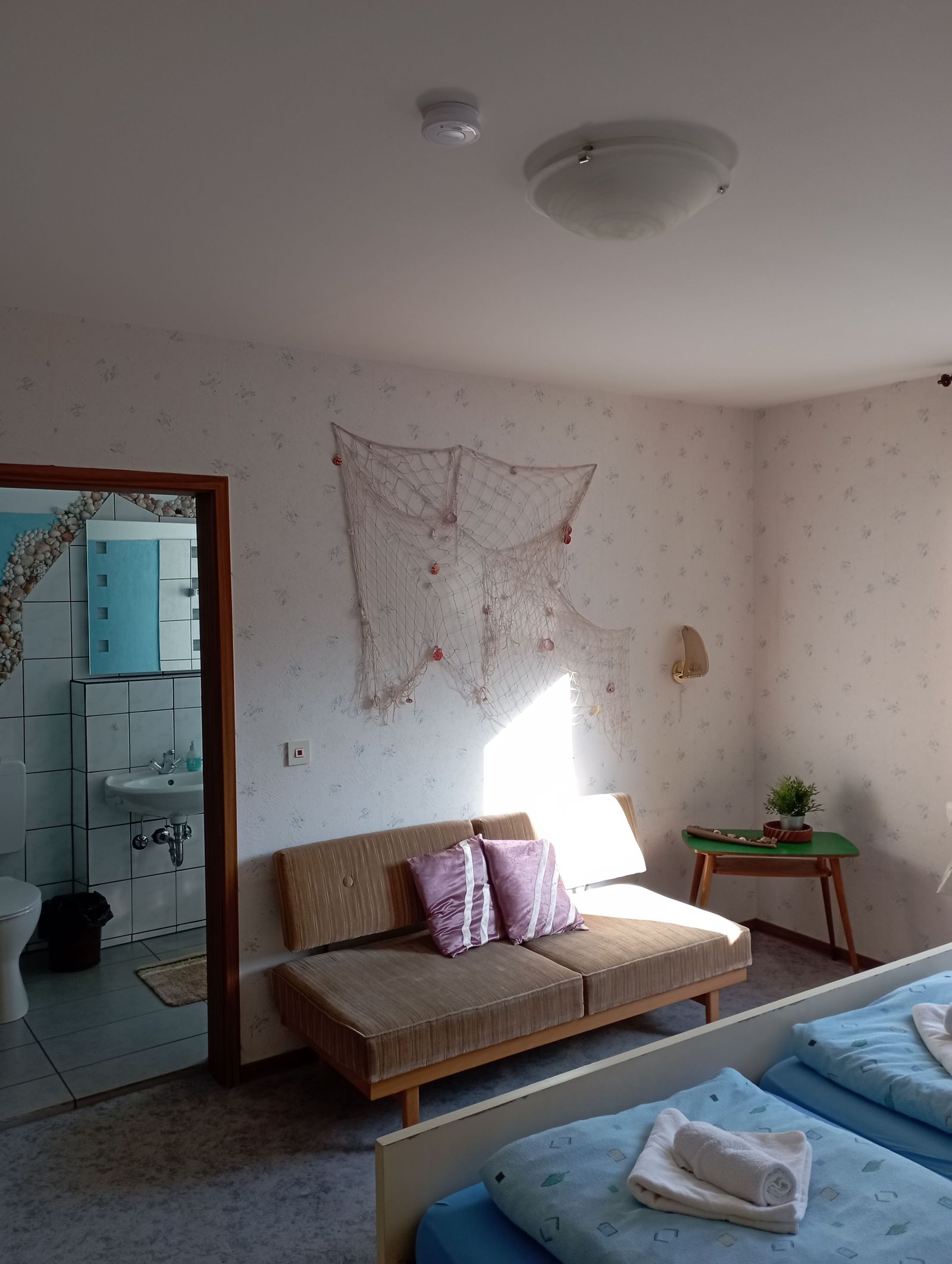 Zimmer mit Sitzecke, Sonnenlicht am Fenster und Blick ins eigene Bad
