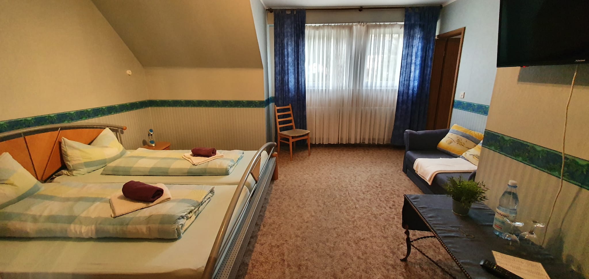 Helles Doppelzimmer mit zwei Betten, Sofa und Fernseher unter der Dachschräge